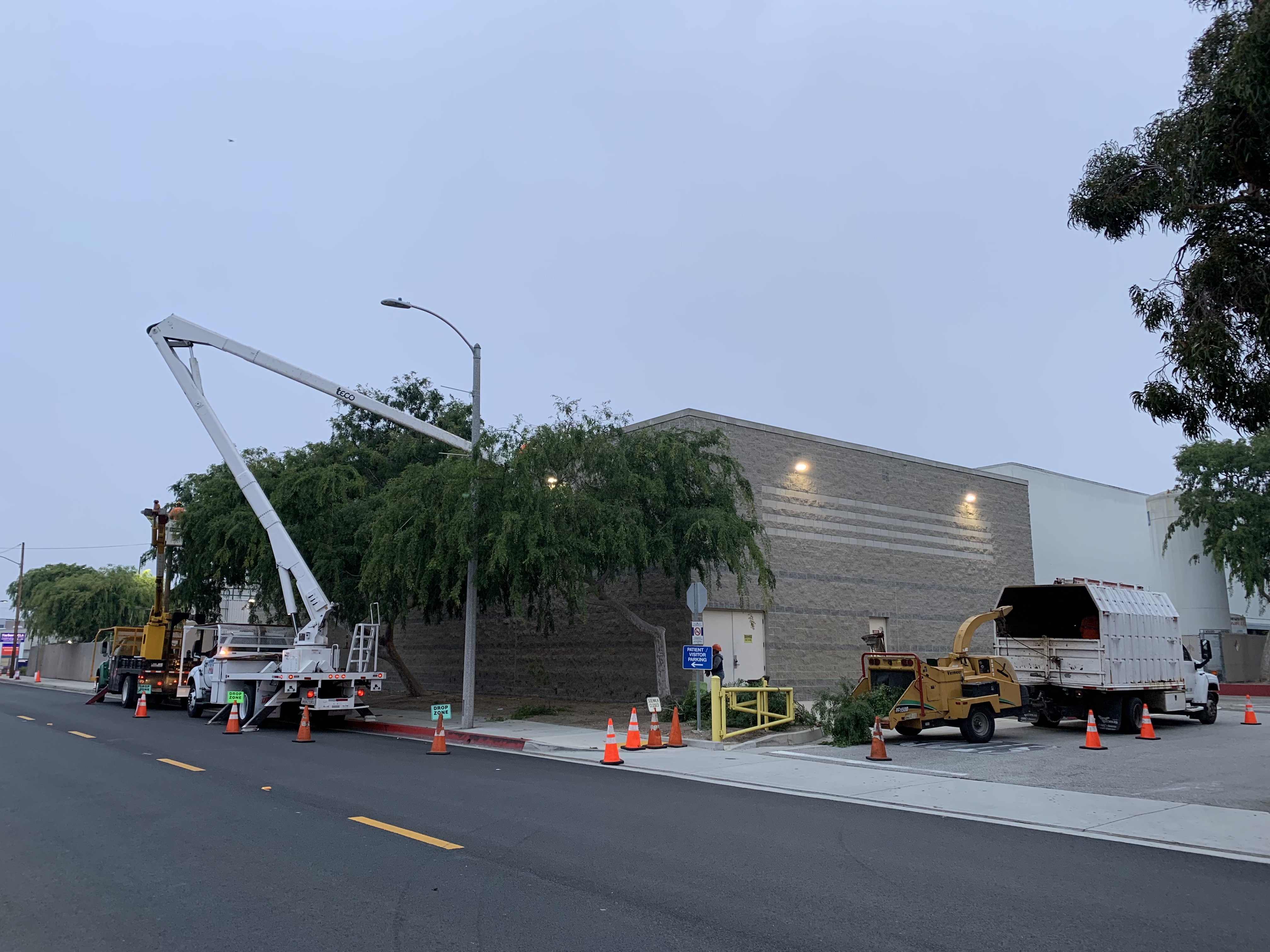 Tiger Tree Services bucket truck and chipper truck operating at dusk on a commercial tree trimming emergency job