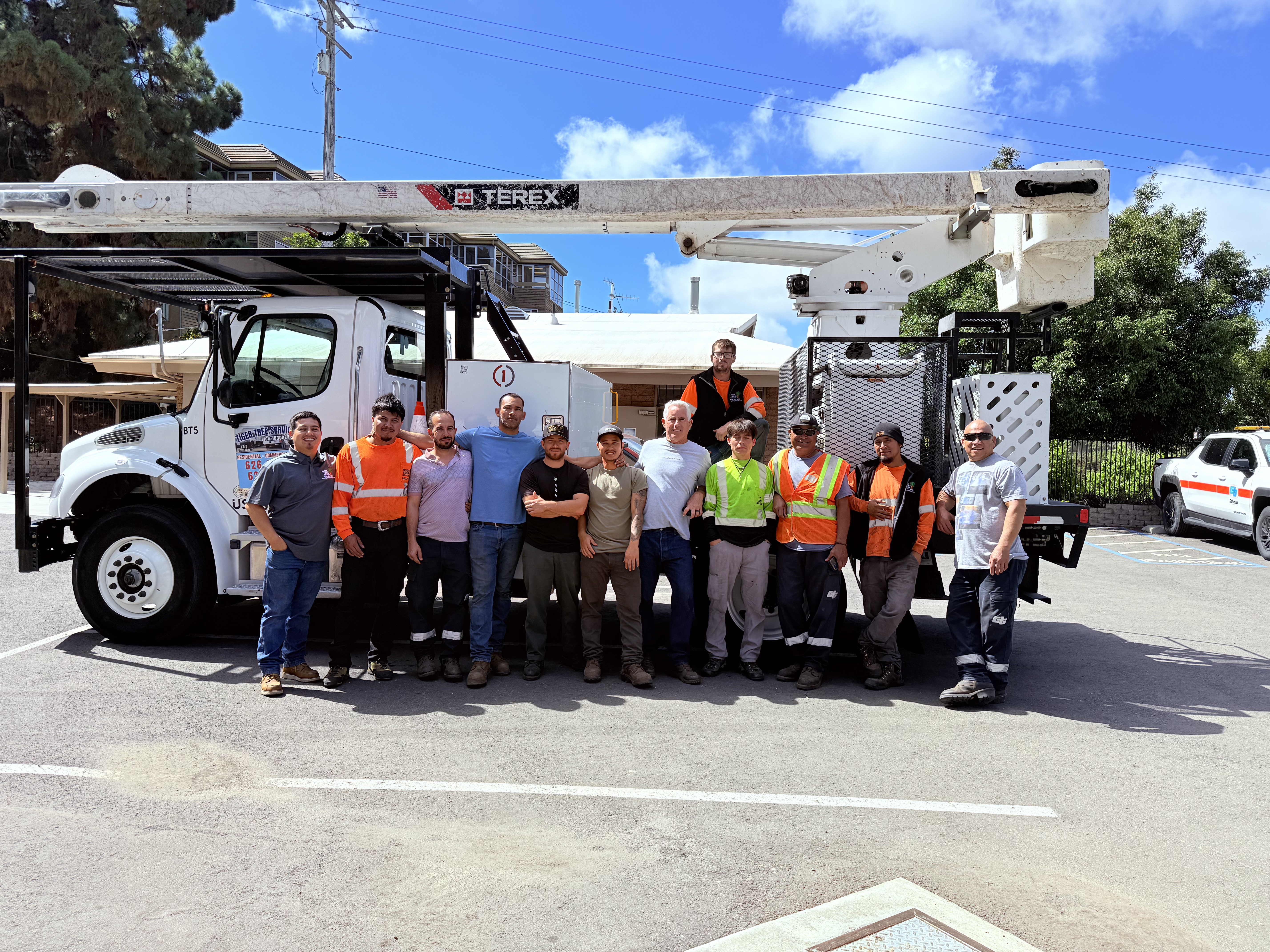 Tiger Tree Services crew of 12 arborists and tree workers in safety gear standing in front of their Terex bucket truck